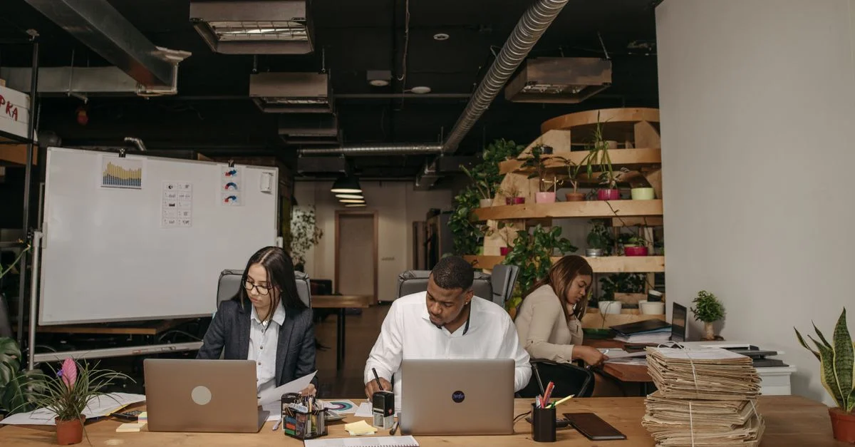 Trois professionnels concentrés sur leur travail dans un bureau élégant avec des ordinateurs portables et des documents.